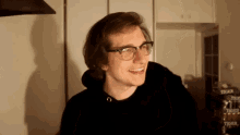 a young man wearing glasses and a black hoodie is laughing .