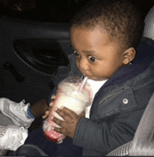 a baby drinking from a cup with a straw in a car