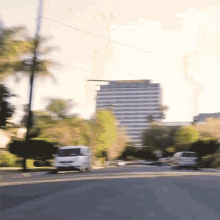 a blurry picture of a street with a white van in the foreground and a tall building in the background