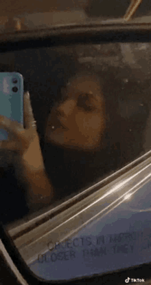 a woman is taking a selfie in the rear view mirror of her car .