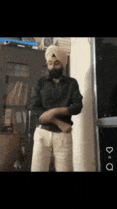 a man wearing a turban and a black shirt is standing in front of a bookcase with binders on it