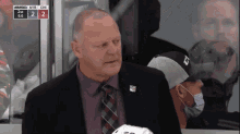 a man in a suit and tie sits in the stands watching a hockey game between the nyr and chi