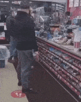 a man in a black hoodie stands in front of a convenience store counter with a sign that says " keep your distance "