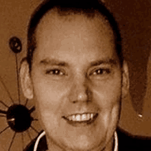 a man in a suit is smiling in front of a clock .