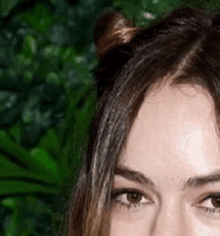 a close up of a woman 's face with a bun in her hair and a green background .