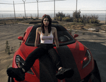 a woman is sitting on the hood of a red car