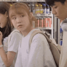 a man and two women are standing next to each other in front of a refrigerator filled with soda .