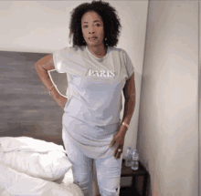 a woman wearing a grey paris t-shirt is standing in front of a bed