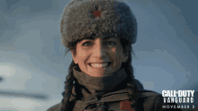 a woman wearing a fur hat is smiling in front of a call of duty vanguard poster