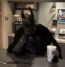 a man in a batman costume sits at a counter with a drink and a napkin dispenser