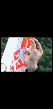 a man with a tattoo on his wrist holds a small object in front of a flag that says ' a ' on it