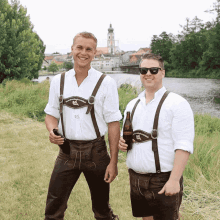 two men standing next to each other with a river in the background and one of them is holding a bottle