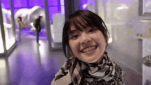 a young woman wearing a scarf is smiling in front of a purple background .