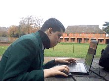 a man in a green jacket is using a laptop outside