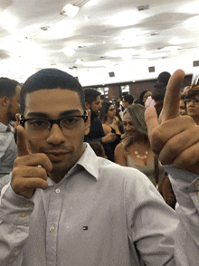 a man wearing glasses and a tommy hilfiger shirt giving a thumbs up