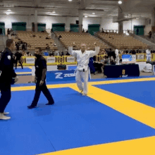 a man in a white karate uniform stands on a blue and yellow mat in front of a sign that says zebra