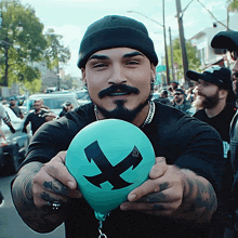 a man with a beard is holding a blue balloon with a black x on it