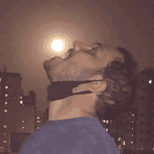 a man with a black mask around his neck looks up at the moon