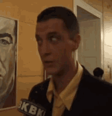 a man in a suit is talking into a microphone in front of a painting of a man .