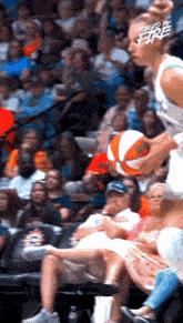 a woman is holding a basketball in front of a crowd at a basketball game sponsored by forged by fire .