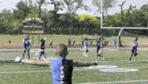 a young boy in a blue and black tank top is standing on a football field with his arms outstretched