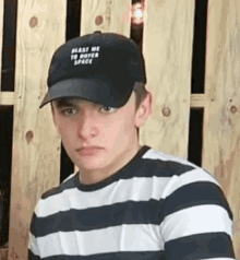 a young man wearing a baseball cap and a striped shirt is sitting in front of a wooden fence .