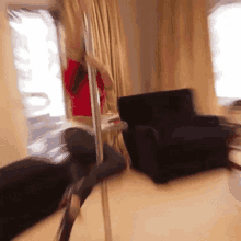 a woman is dancing on a pole in a living room next to a chair .