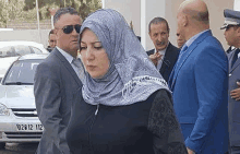 a woman in a hijab is standing next to a man in a suit and sunglasses .