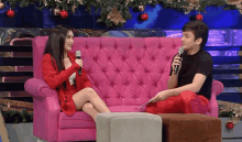 a man is holding a microphone and talking to a woman on a pink couch