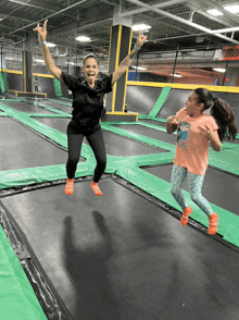 a woman and a girl are jumping on a trampoline in a gym