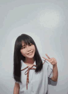 a young girl in a school uniform is giving the peace sign