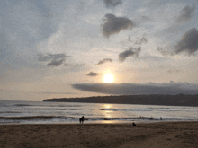 a sunset over a beach with a few people walking on the sand