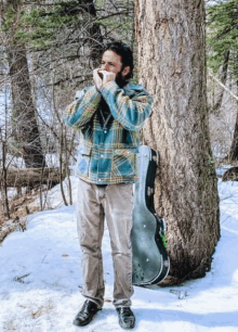 a man playing a harmonica while standing next to a tree