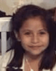 a young girl is smiling for the camera while sitting in a chair in a blurry photo .