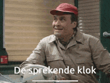 a man wearing a red hat is sitting at a desk with the words de sprekende klok written below him