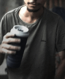 a man in a gray shirt is holding a black cup of coffee