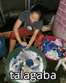 a woman is sitting on the ground washing clothes in a large bowl .