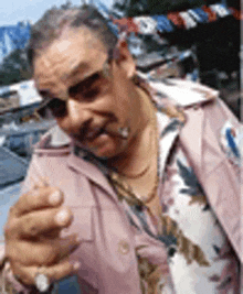 a man wearing sunglasses and a pink jacket is smoking a cigarette in front of a car .