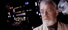 an older man with a beard looks at the camera with a blurred background and a few lights behind him