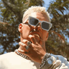 a man wearing sunglasses , a necklace , a watch and a ring on his finger .