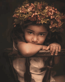 a little girl with a flower crown on her head leaning on a chair