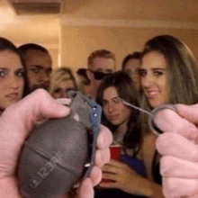 a group of people are standing around a woman holding a grenade in her hand .