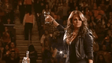 a woman in a leather jacket is holding a glass of wine in front of a crowd of people .