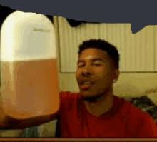 a man in a red shirt is holding a gallon of orange liquid .