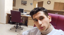 a man taking a selfie in an office with a clock on the wall above him