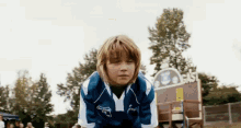 a young boy wearing a blue and white jersey with the letter y on it stands in front of a sign that says gas