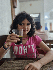 a girl in a pink shirt that says do n't is holding a glass of soda