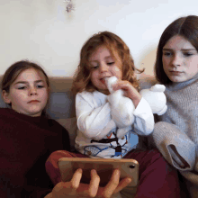 three young girls are sitting on a couch looking at a phone