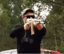 a man wearing sunglasses and a hat is holding a gun in his hands .