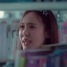 a woman wearing a headband with a star on it is standing in front of a shelf of books .